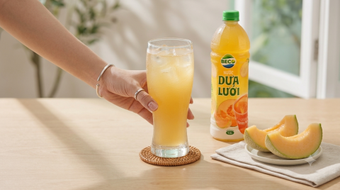 Ly nước dưa lưới lạnh đặt trên bàn gỗ sáng màu cùng những miếng dưa lưới tươi